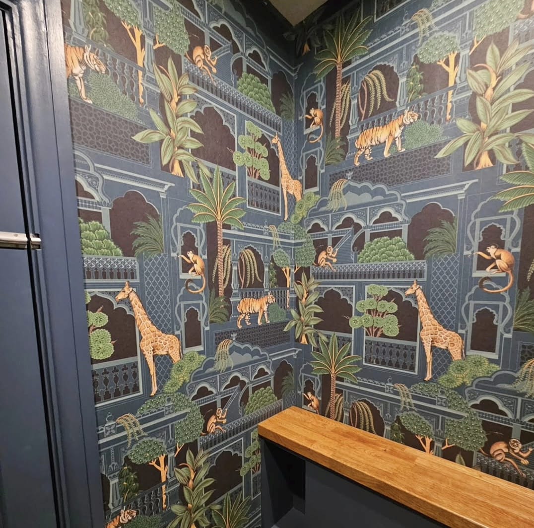 Cloakroom hung in blue jungle arches wallpaper with tigers and giraffes