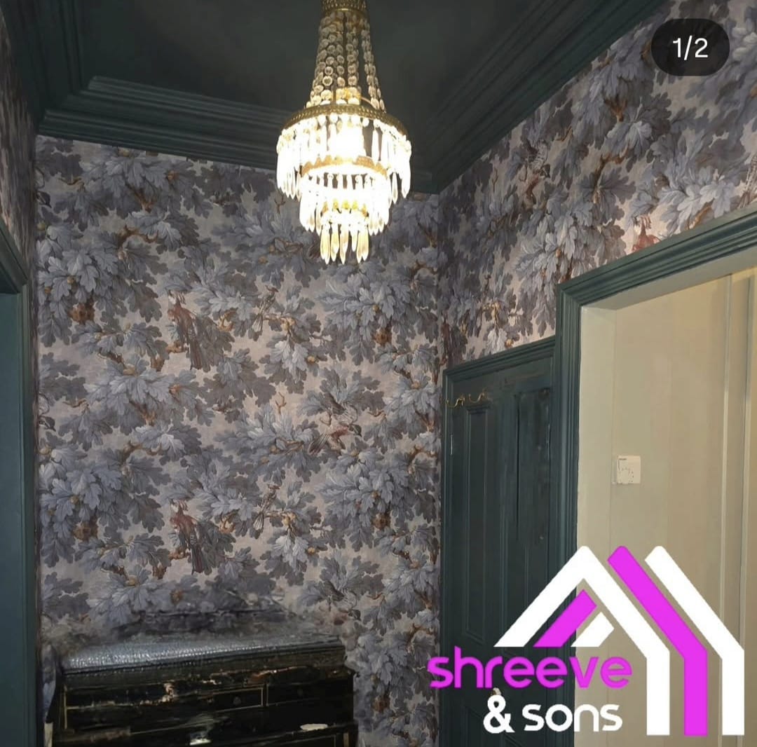 Hallway with oak leaf and bird wallpaper, dark green painted woodwork and chandelier